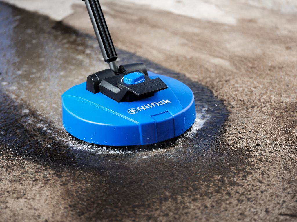 Blue Nilfisk pressure washer attachment cleaning concrete terrace, spraying water to remove grime.