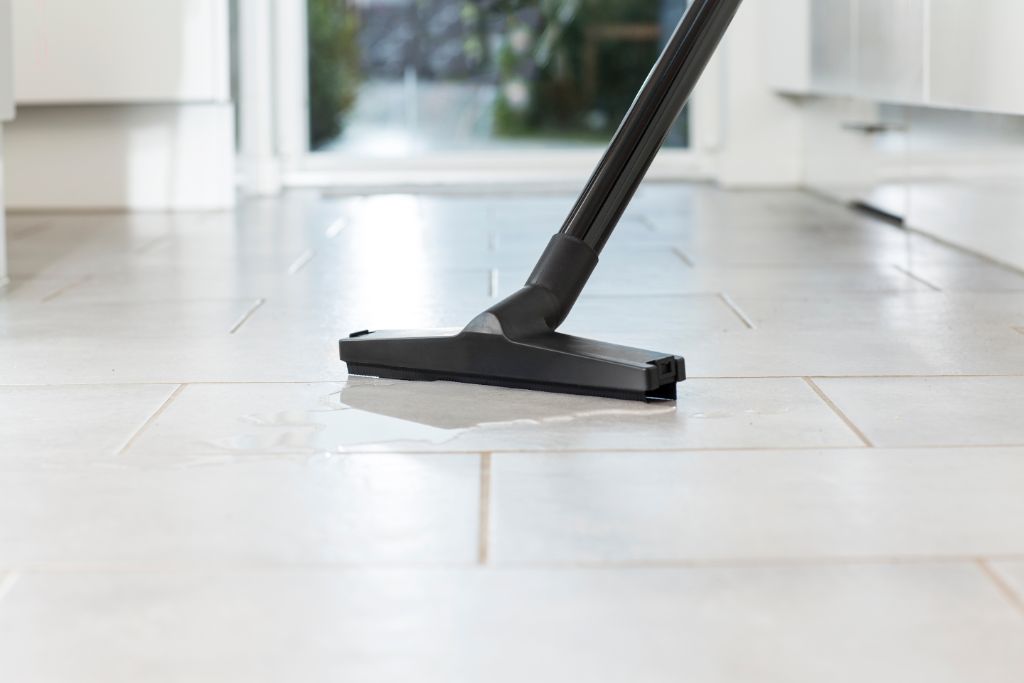Black wet/dry vacuum head cleaning spilled water on light tile floor in bright kitchen.
