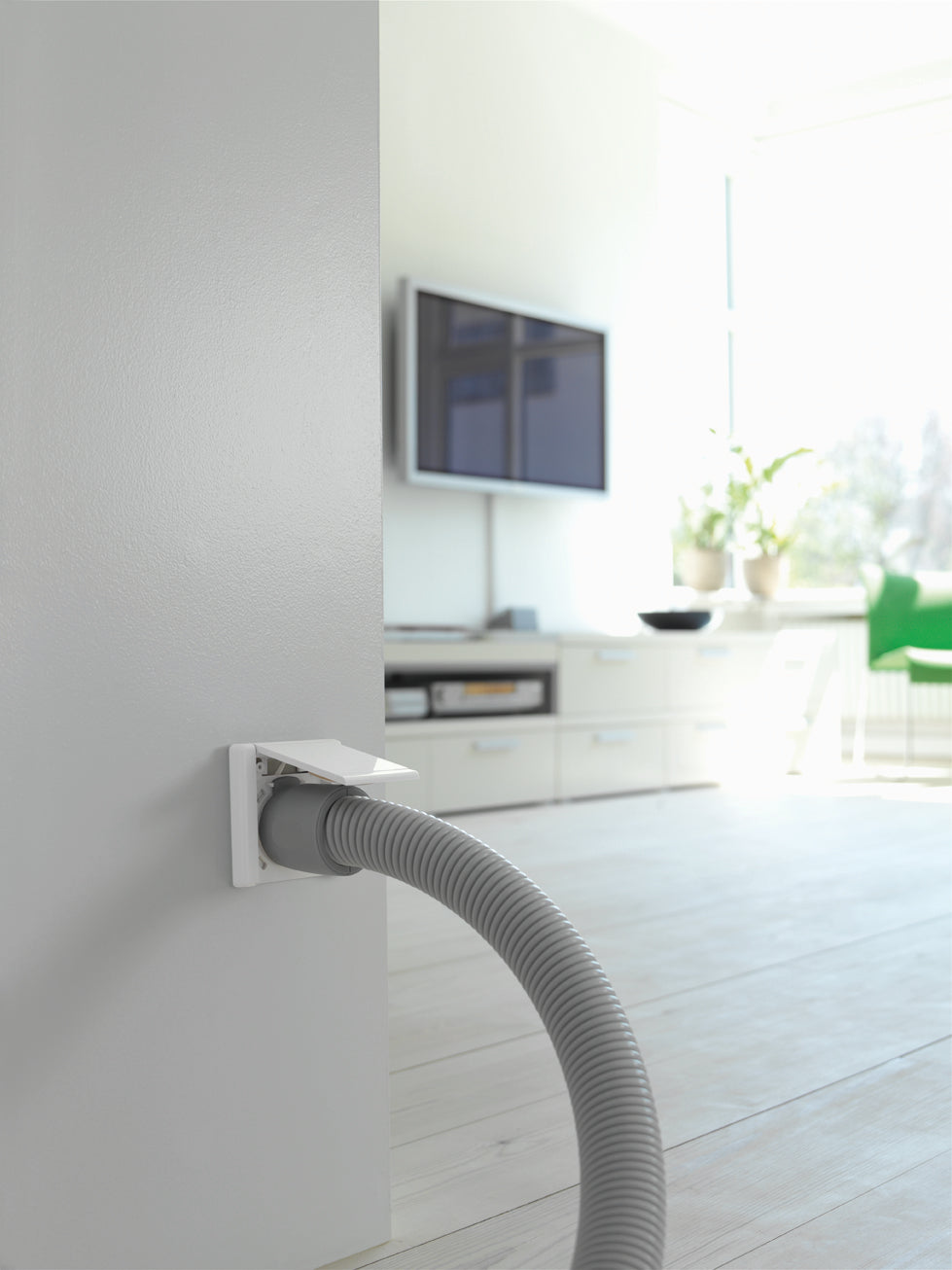 Gray vacuum hose connected to wall outlet in bright, modern living room with TV and green chair.