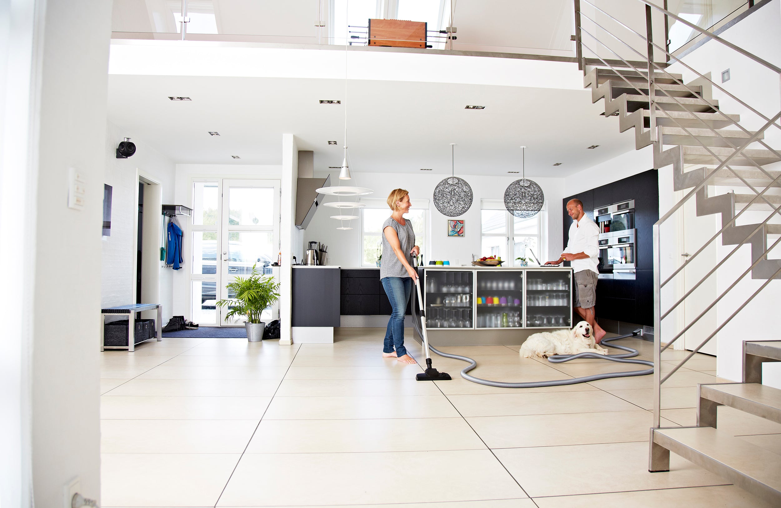 Modern open-plan kitchen with couple cleaning, dog resting, sleek design, and natural light.