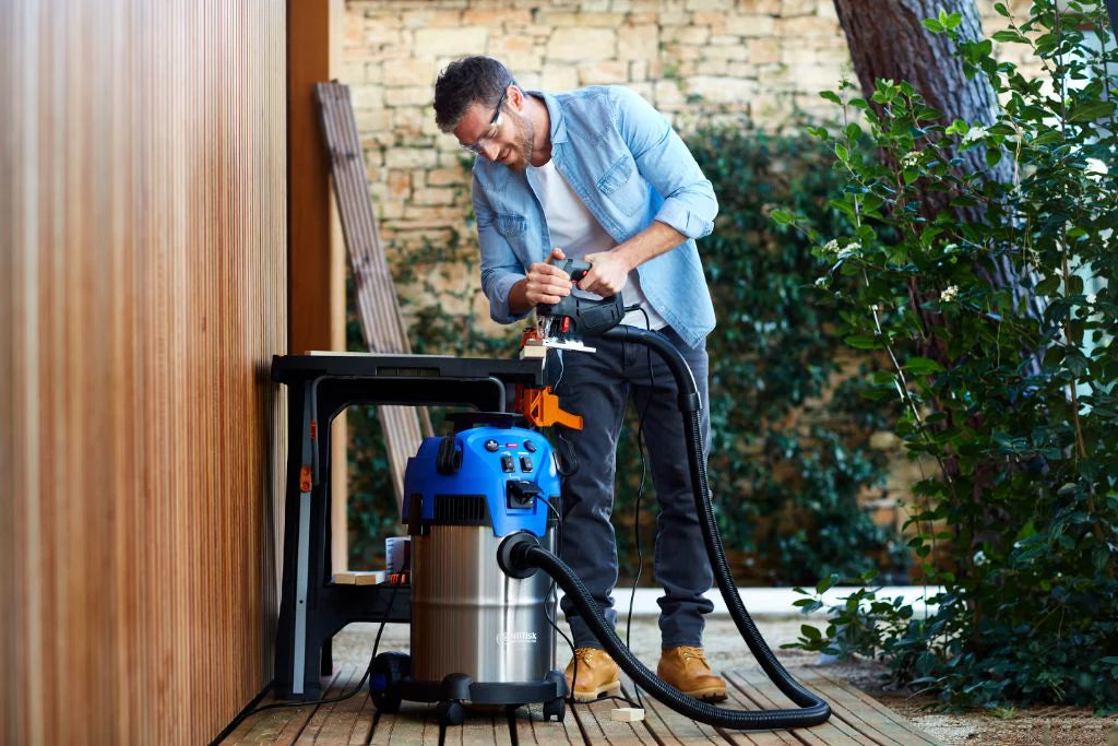 Man using wet/dry vacuum while woodworking outdoors, efficiently cleaning sawdust from workshop area.
