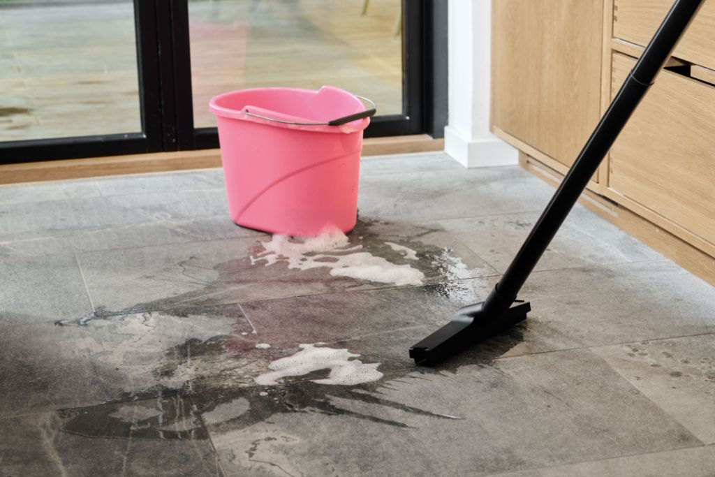 Black wet/dry vacuum cleaning soapy water spill on gray tile floor near pink bucket.
