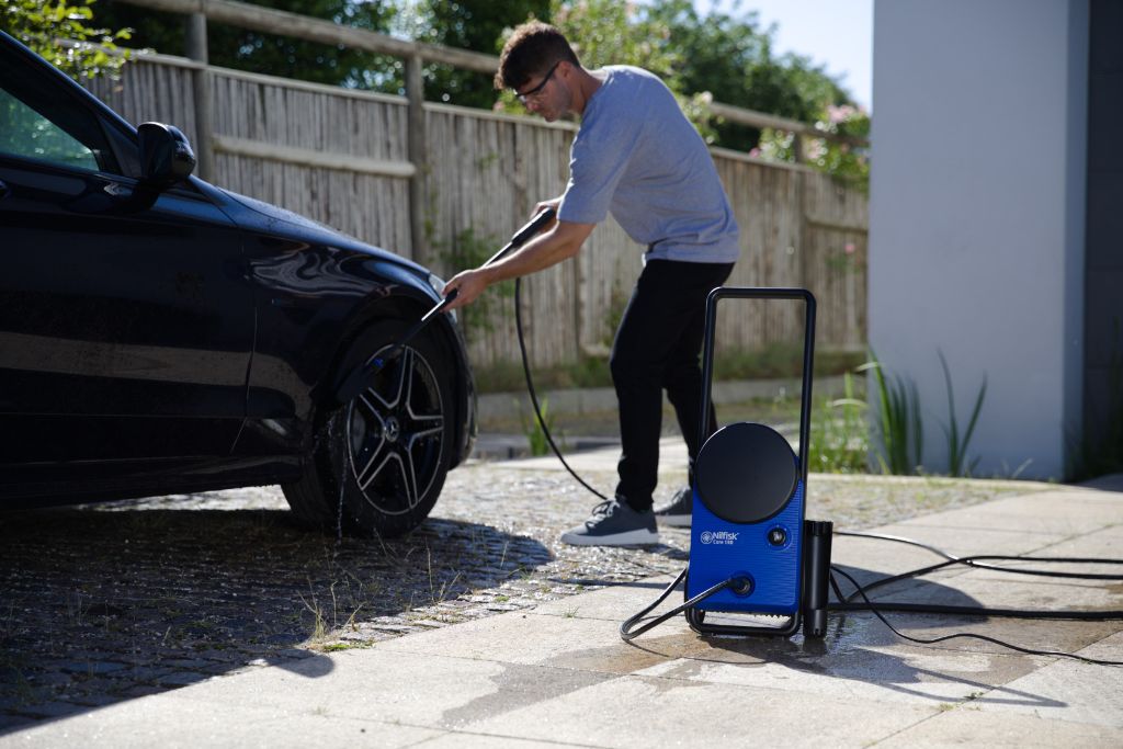 Blue high pressure washer by Nilfisk with black handle, next to a man washing a black car.