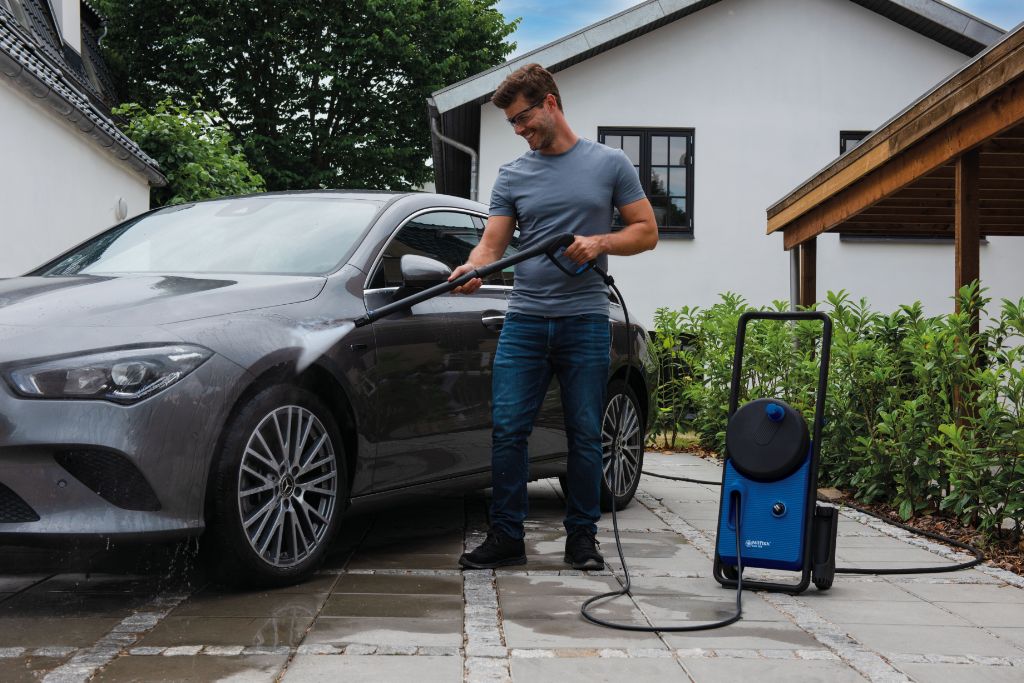 High pressure washer Core 150-10 PowerControl UK by Nilfisk, being used to wash a car, outdoors on a paved driveway.
