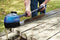 Blue power brush by Nilfisk cleaning a weathered wooden picnic table.