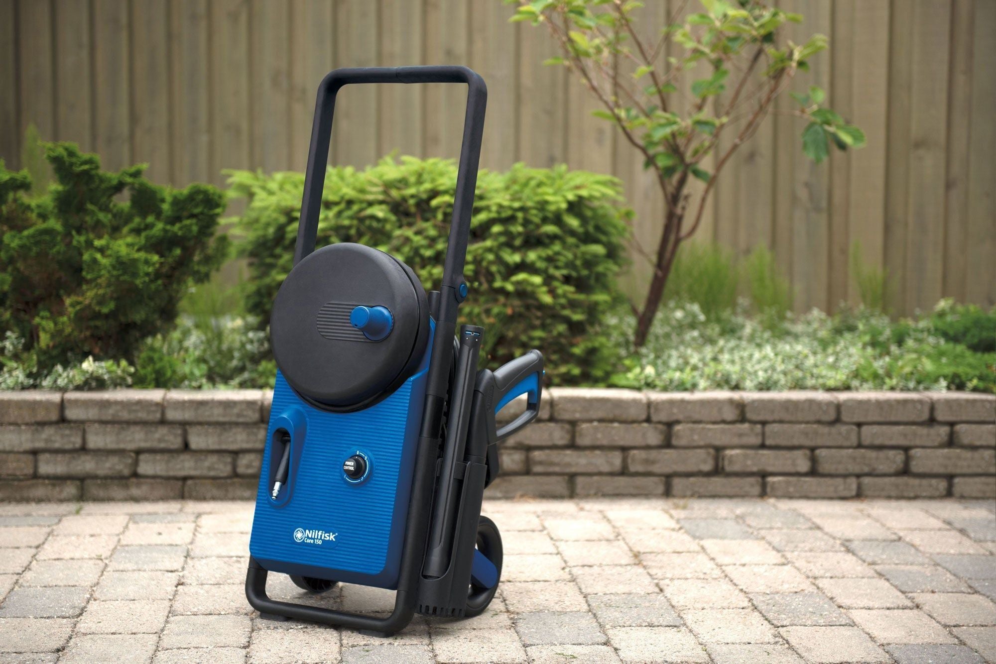 Blue and black pressure washer by Nilfisk Core 150, standing outdoors on a paved surface.
