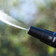 High-pressure washer by Nilfisk with a black nozzle spraying water against an out-of-focus green backdrop.