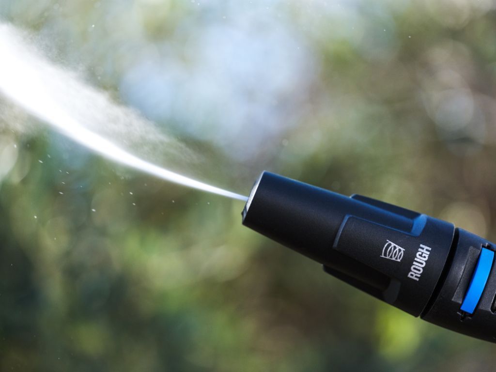 High-pressure washer by Nilfisk with a black nozzle spraying water against an out-of-focus green backdrop.
